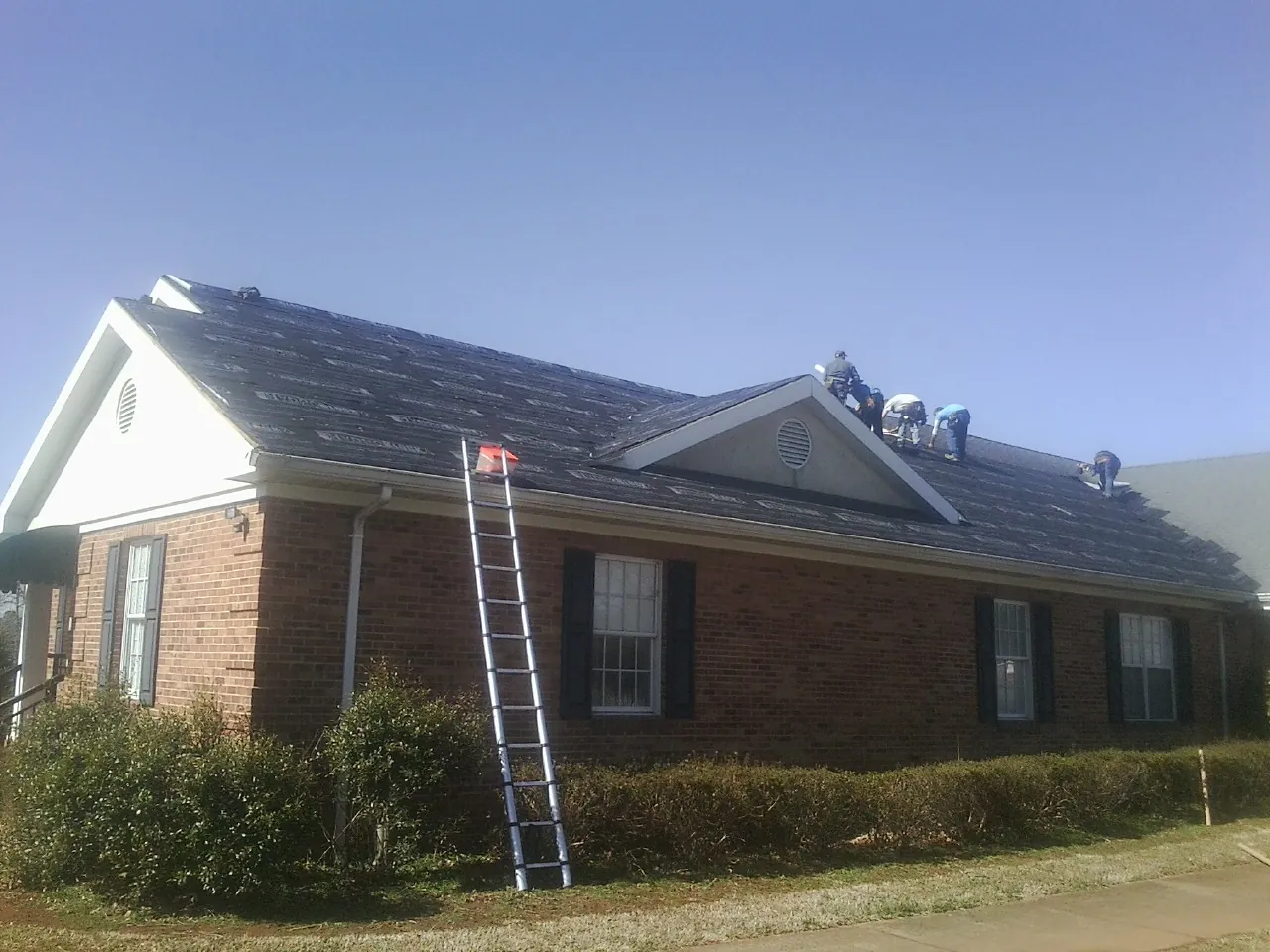 Crew tearing shingles off a brick ranch roof with a ladder set — Emergency Roof Repair work by our crew in Climax
